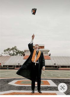 a man in a graduation gown and orange scarf flying a kite on the football field