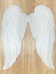 two white angel wings sitting on top of a wooden floor