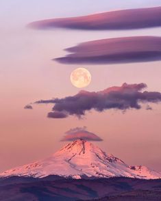 the moon is setting over a mountain with clouds in the foreground and pink sky above it