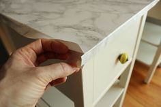 a person holding something in their hand near a white table with drawers on both sides