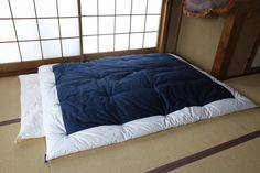 an empty bed in a room with tatami mats on the floor and large windows