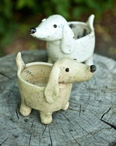 two small ceramic dogs sitting on top of a wooden stump in front of some trees