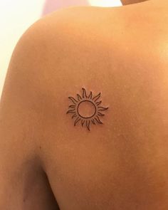 the back of a woman's shoulder with a small sun tattoo on it