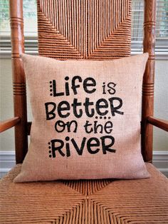 a chair with a pillow that says life is better on the river in black lettering