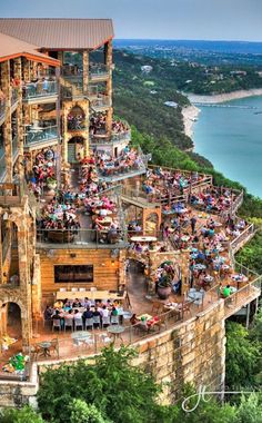 an aerial view of people sitting at tables on the side of a building with water in the background