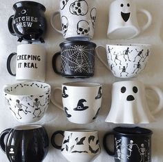 a collection of halloween themed coffee mugs on a white tablecloth with black and white designs