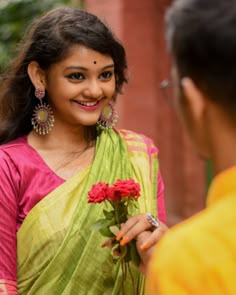 a woman in a green sari holding a red rose and smiling at another woman