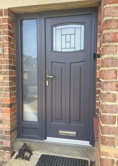 the front door to a house with a black mat on the ground and brick wall behind it