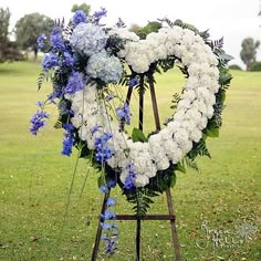 a heart shaped wreath with blue and white flowers in the center on a easel