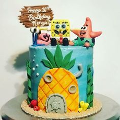 a birthday cake decorated with spongebob characters and pineapple on a table in front of a white wall