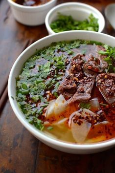 a bowl filled with meat and vegetables on top of a wooden table next to bowls of soup