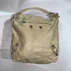 beautiful, authentic, BALENCIAGA cream distressed goat skin leather Moto City Day Bag. Features signature buckle and mesh stud detailing at the front, single whipstitched leather strap at the shoulder. Fully liked in black cotton, with one interior sidewall zip secure pocket. Includes sleeper bag and original BALENCIAGA mirror. VERY GOOD PRE-OWNED CONDITION, shows normal use appropriate signs of wear and tear including patination to the leather from being handled, light dirt marks to exterior from normal use and light ink mark or two at exterior which are not noticeable unless looking for them. APPROXIMATE MEASUREMENTS 16" x 5" x 13" 10" Strap drop MADE IN ITALY RETAIL $2600 Balenciaga Metallic Edge City, Balenciaga Monogram Bag, Balenciaga Bag Silver, Balenciaga City Bag 2000s, Balenciaga Motorcycle Bag Brown, Leather Moto, Day Bag, Black Cotton, Bags Handbags