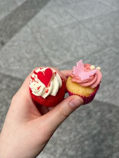 a hand holding two cupcakes with white frosting and red sprinkles