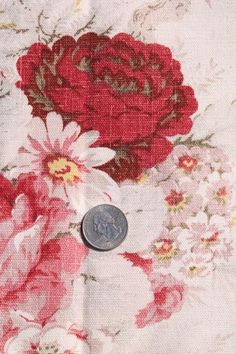 a penny sitting on top of a flowered fabric with red and white flowers all over it