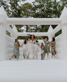 a group of women standing around each other in front of a white structure with trees