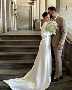 a bride and groom standing on the steps in front of some stairs holding their bouquet