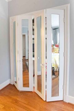 an empty room with mirrored doors and hardwood flooring in the corner, looking into another room