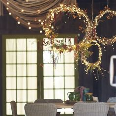 a dining room table with chairs and lights hanging from it's ceiling in front of an open window