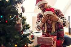 a man giving a woman a christmas present in front of a christmas tree with presents