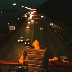 a person standing on a balcony looking at the street and cars going by in the distance