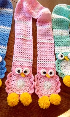 three crocheted owls are sitting on a table next to two knitted scarves