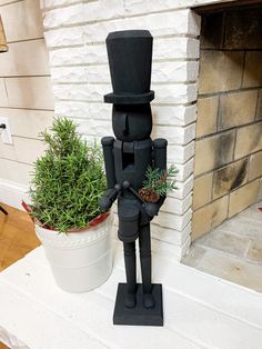 a black statue with a top hat and cane next to a potted plant in front of a fireplace