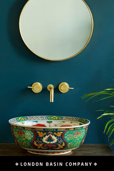 a bathroom sink sitting under a mirror next to a potted green plant in front of a blue wall