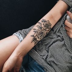 a woman with a flower tattoo on her arm holding a cell phone in her hand