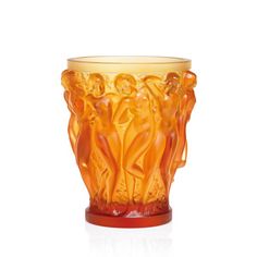 an orange glass vase sitting on top of a white surface with two figures in the center