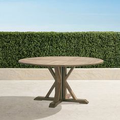 a wooden table sitting on top of a cement floor next to a hedge covered wall