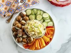 a bowl filled with assorted vegetables on top of a white marble counter next to utensils