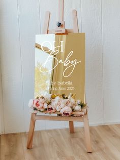 an easel with flowers on it in front of a white wall and wooden floor