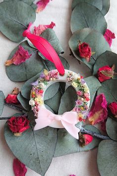 a wreath made out of flowers and leaves on a table with pink ribbon hanging from it