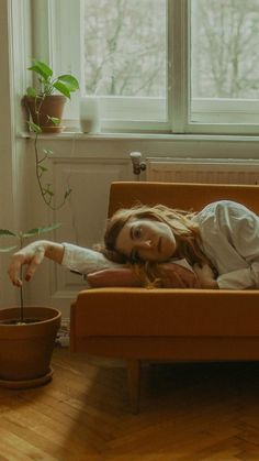 a woman laying on top of a couch next to a potted plant in front of a window