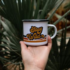 a hand holding a coffee cup with the words stay wild on it in front of some plants