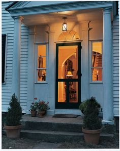 the front door of a white house with potted plants