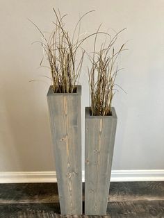 two tall wooden vases with plants in them on the floor next to a wall