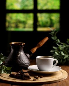 a cup and saucer sitting on a wooden table next to a potted plant