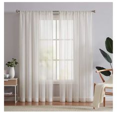 a white curtain hanging on the side of a window next to a chair and potted plant