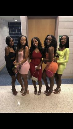 four beautiful young women standing next to each other in front of a bathroom door wearing short dresses