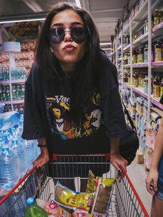 a woman in sunglasses is standing behind a shopping cart with food and drinks on it