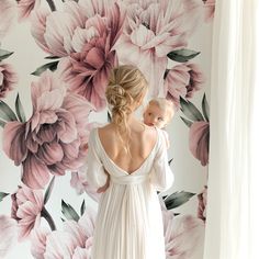 a woman holding a baby in front of a floral wallpapered room with pink flowers