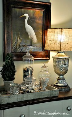 a white bird sitting on top of a table next to a lamp and vases