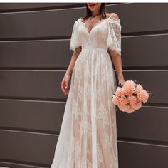 a woman in a white dress is holding a bouquet and standing next to a wall