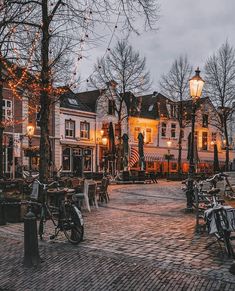 an outdoor area with tables, chairs and bicycles in front of buildings at night time