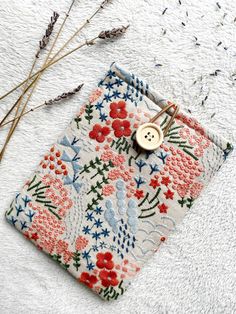 a white and red flowered bag with a button on it next to dried flowers