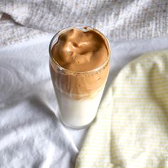 a glass filled with liquid sitting on top of a white bed sheet next to a yellow and white blanket