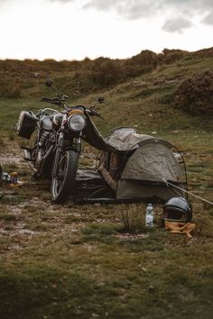 a motorcycle parked next to a tent on top of a grass covered field with other items