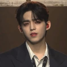 a young man in a suit and tie looks at the camera while wearing ear rings