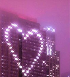 a large building with many lights on it's side and some buildings in the background